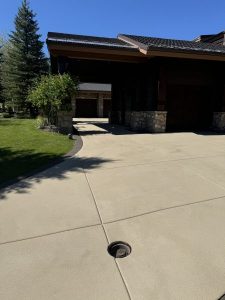 A Resin Rock driveway with a round metal drain in the center leads to a garage attached to a house with stone columns and a lawn on the left.