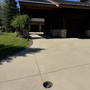 A Resin Rock driveway with a round metal drain in the center leads to a garage attached to a house with stone columns and a lawn on the left.