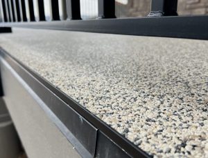 Close-up view of a textured, pebble-like Resin Rock surface next to a black metal railing, with the image focused on the surface detail.