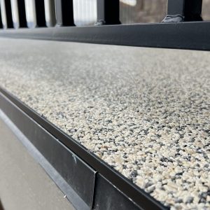 Close-up view of a textured, pebble-like Resin Rock surface next to a black metal railing, with the image focused on the surface detail.