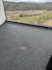 A balcony with a Resin Rock speckled gray floor and a central drain overlooks a landscape of hills, buildings, and a river in the background.