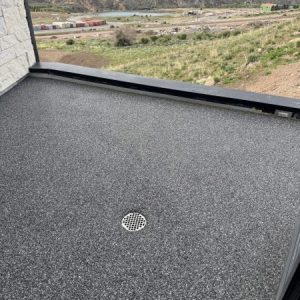 A balcony with a Resin Rock speckled gray floor and a central drain overlooks a landscape of hills, buildings, and a river in the background.