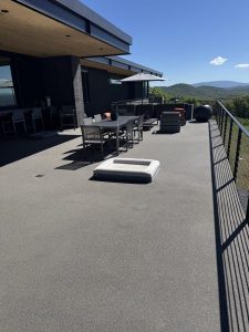 A spacious rooftop patio with Resin Rock outdoor furniture and railing, overlooking hills under a clear blue sky.