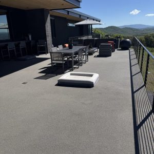 A spacious rooftop patio with Resin Rock outdoor furniture and railing, overlooking hills under a clear blue sky.