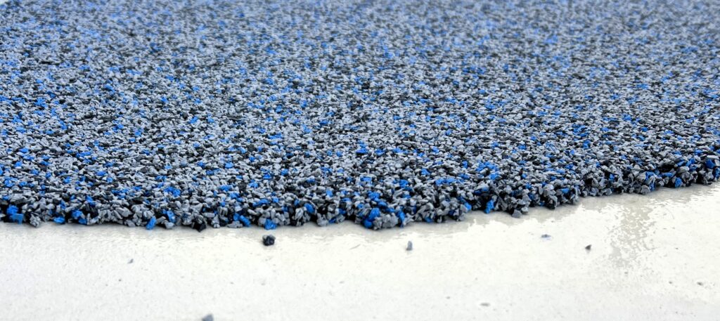 Close-up of a textured blue and gray Resin Rock rubber surface on a white background, highlighting the rough edge where the material ends.
